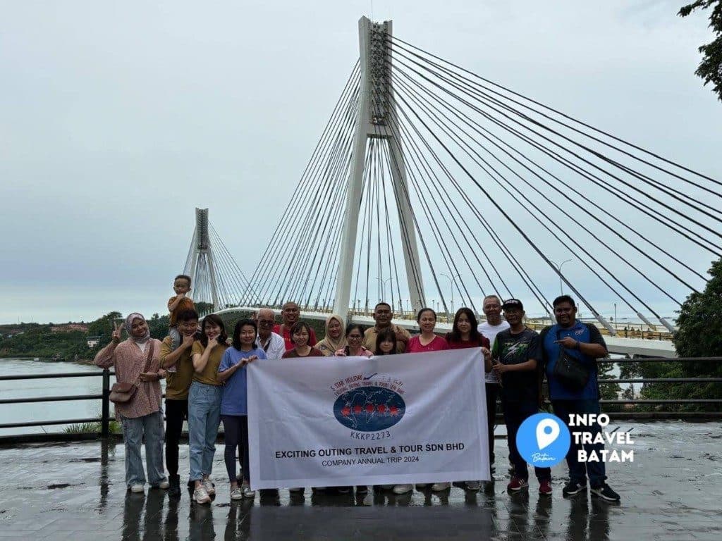 A tour group holding an Exciting Outing Travel and Tour banner at the Barelang Bridge viewpoint in Batam