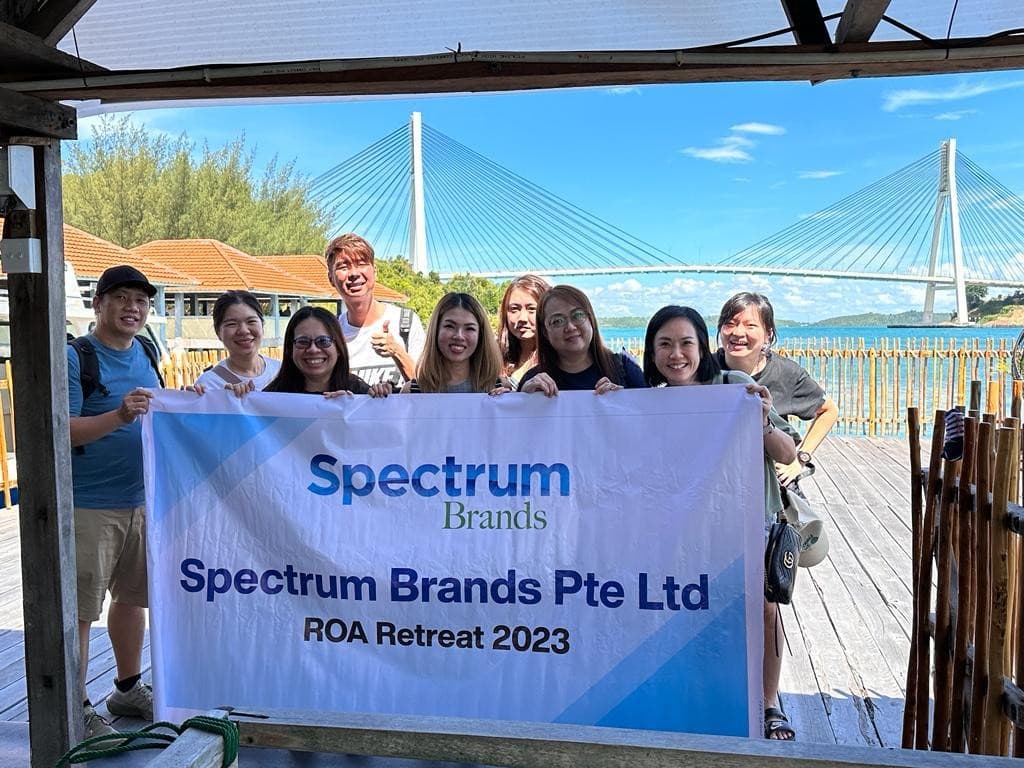 A company group holding a Spectrum Brands retreat banner on a jetty, the Barelang Bridge behind them